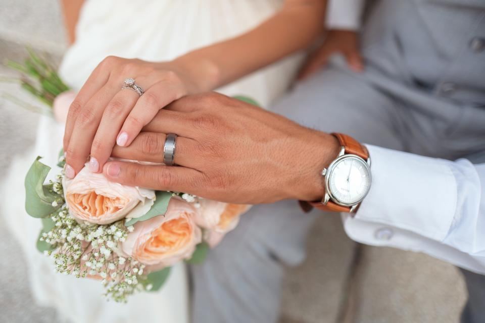 Manos de novios con anillos sobre un ramo de flores